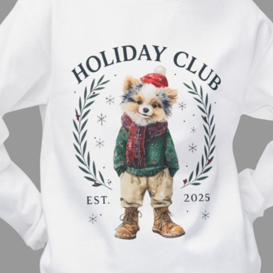 White sweatshirt with a festive design featuring a dog in a green sweater and red scarf, surrounded by wreaths and text on a gray background.