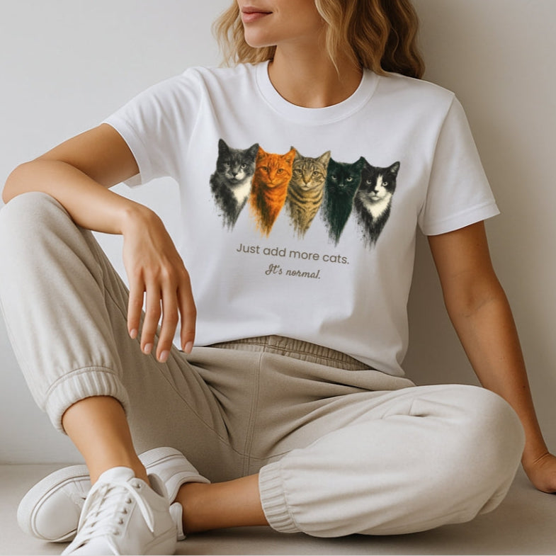 Woman wearing a white t-shirt with cat illustrations and text, sitting on a light-colored floor.