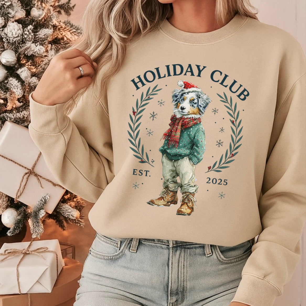 Person wearing a beige sweatshirt with a 'Holiday Club' design, sitting in front of a Christmas tree and presents.