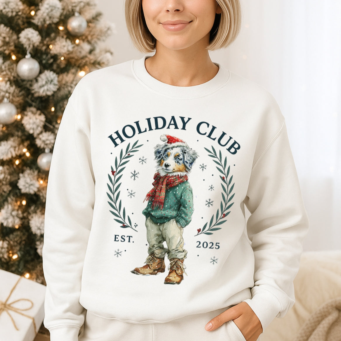 Woman wearing a white sweatshirt with 'Holiday Club' design in front of a decorated Christmas tree.