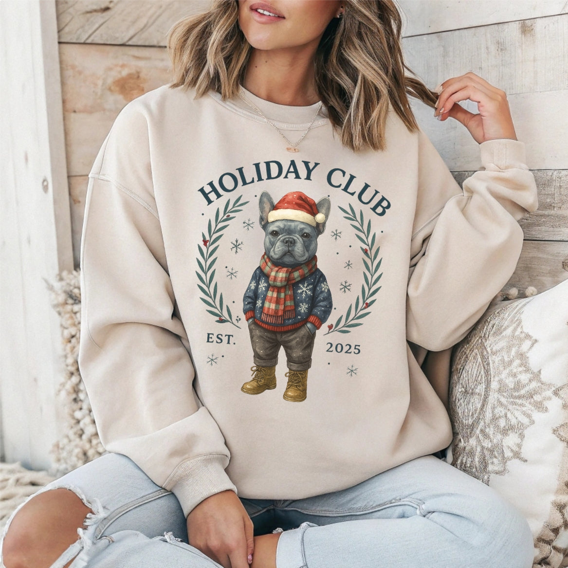 Person wearing a beige sweatshirt with a dog graphic and 'Holiday Club' text, sitting on a wooden floor.