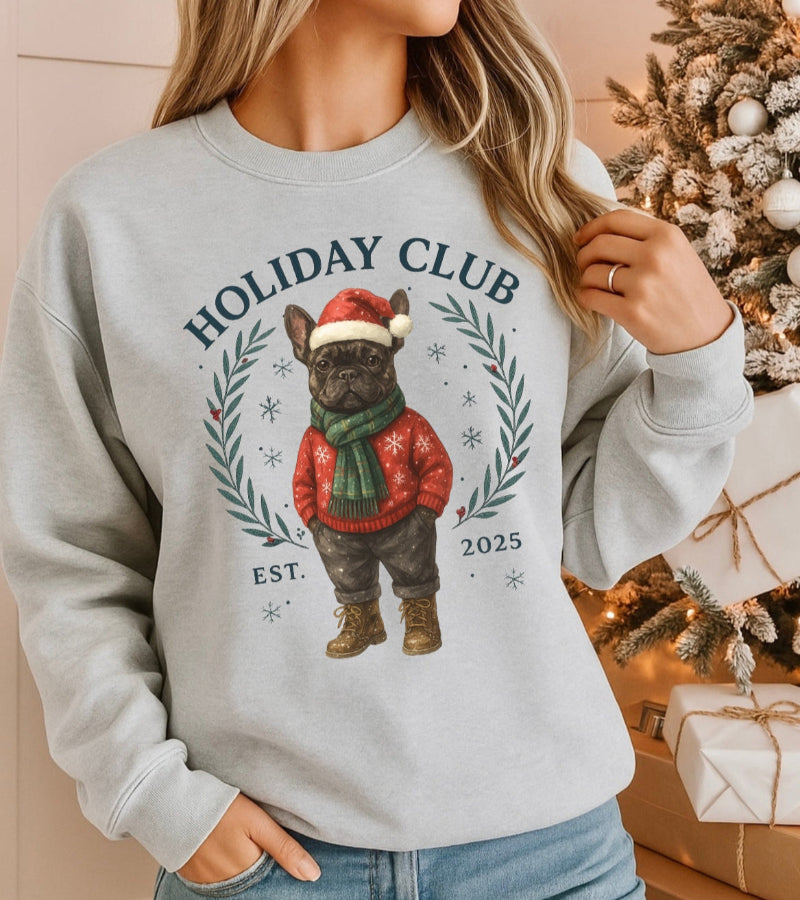 Person wearing a gray sweatshirt with a Christmas-themed design featuring a dog in a red sweater and Santa hat, with a decorated Christmas tree in the background.