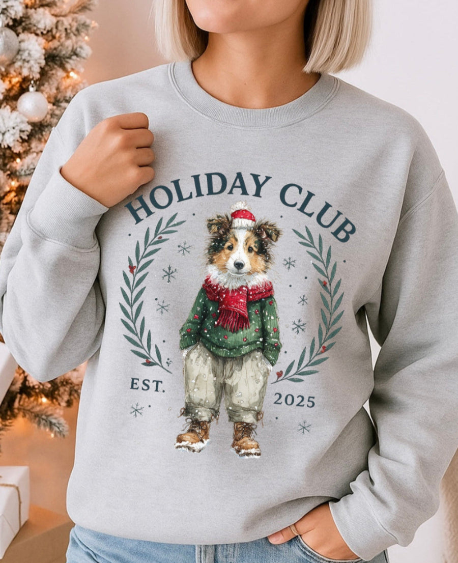Person wearing a gray sweatshirt with a dog illustration and 'Holiday Club' text, Christmas tree in the background