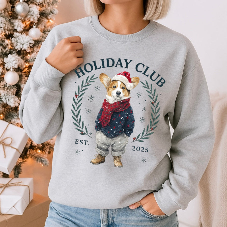 Person wearing a gray sweatshirt with a holiday-themed design featuring a dog and 'Holiday Club' text, standing in front of a decorated Christmas tree.