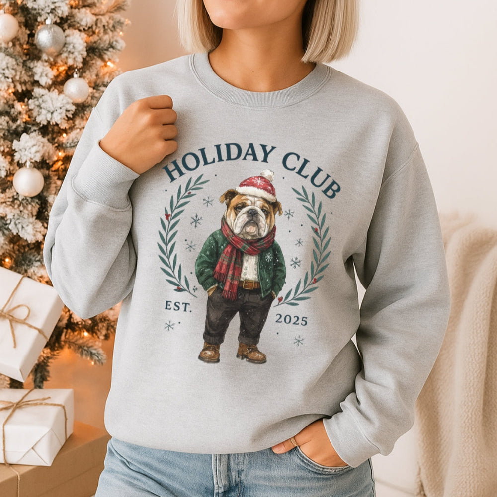 Woman wearing a gray sweatshirt with a dog graphic and 'Holiday Club' text, standing in front of a decorated Christmas tree.