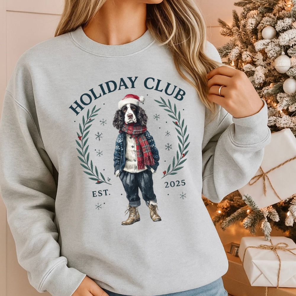 Person wearing a gray sweatshirt with a holiday-themed design featuring a dog, in front of a decorated Christmas tree.