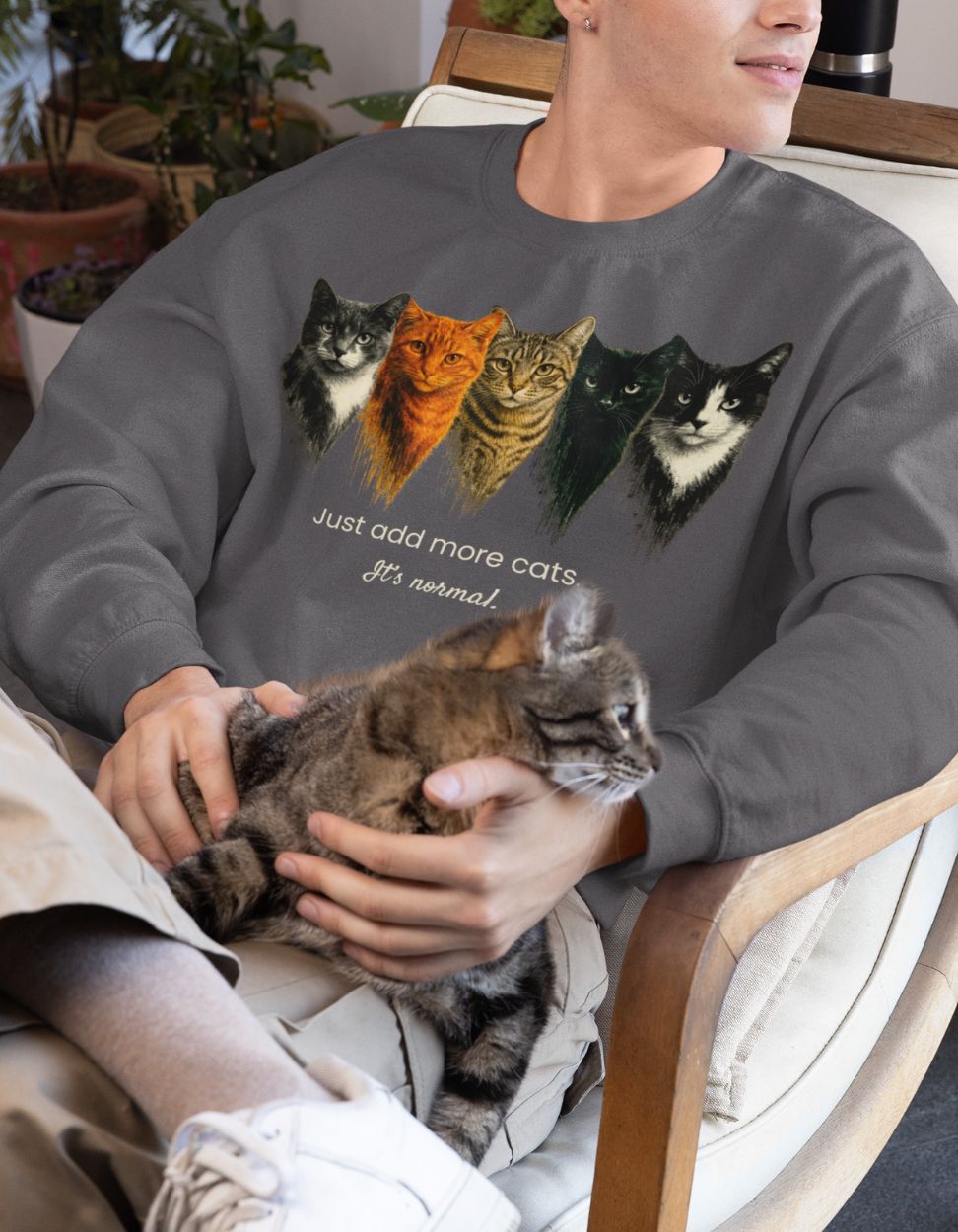 Person wearing a asphalt color sweatshirt with cat illustrations and text, holding a cat.
