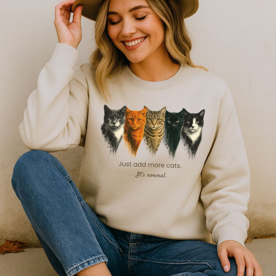 Woman wearing a cream sweatshirt with cat illustrations and text, sitting on a beige couch.