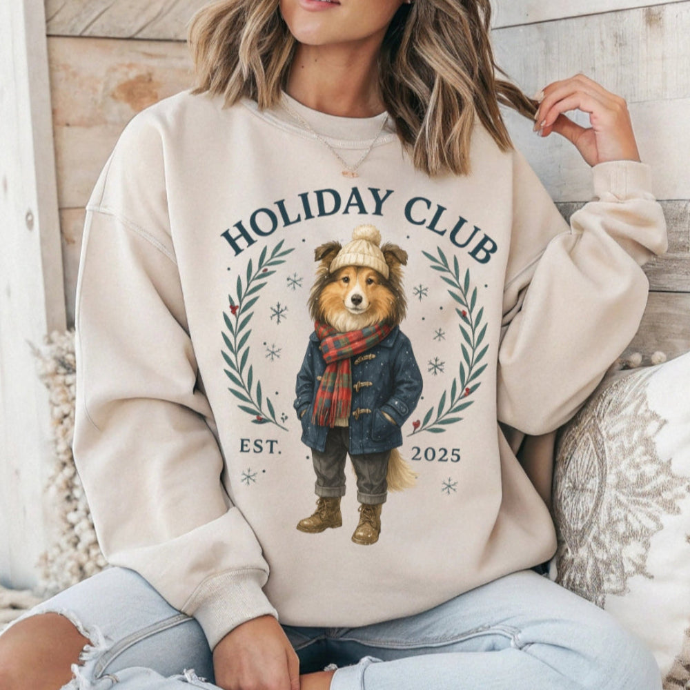 Person wearing a beige sweatshirt with a bear graphic and 'Holiday Club' text, sitting on a wooden floor.