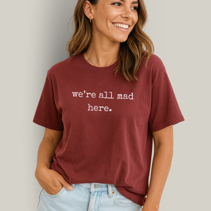 Woman wearing a maroon t-shirt with 'we're all mad here.' text against a plain background