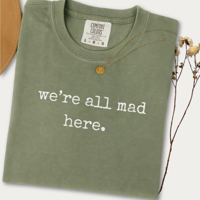 Green t-shirt with 'we're all mad here' text on a white background