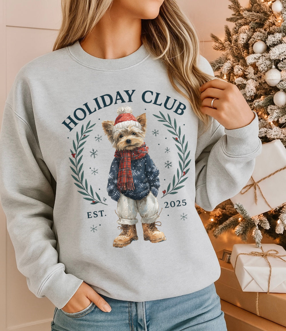 Person wearing a gray sweatshirt with a dog graphic and 'Holiday Club' text, standing in front of a decorated Christmas tree.