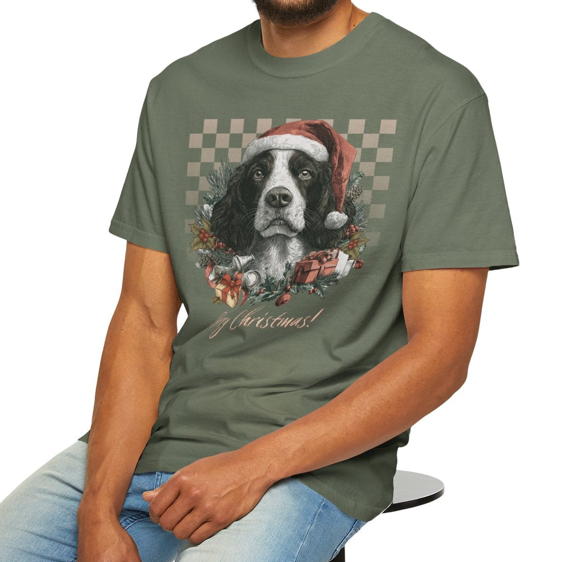 Man wearing a green t-shirt with a dog graphic, sitting on a stool against a white background