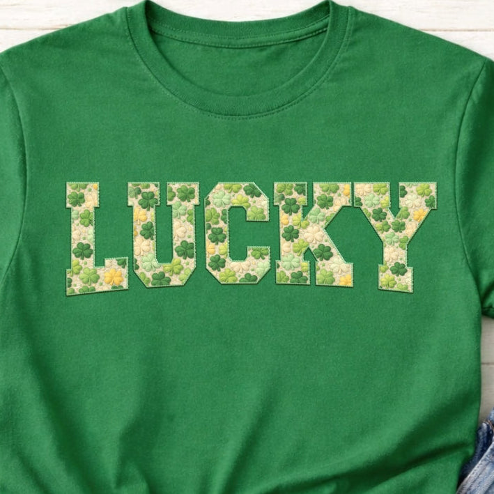Green t-shirt with 'LUCKY' text made of clover leaves on a wooden surface.