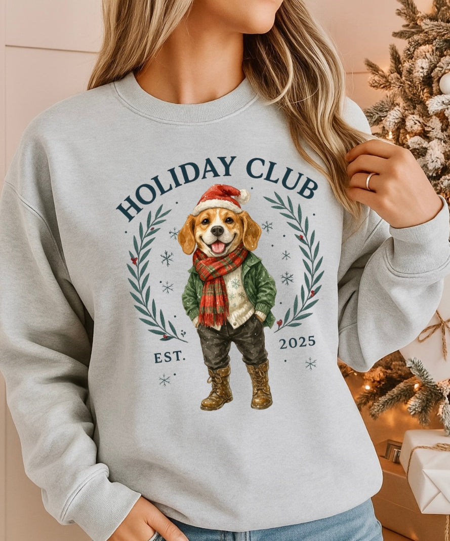 Person wearing a gray sweatshirt with a holiday-themed design featuring a dog and 'Holiday Club' text, standing in front of a decorated Christmas tree.