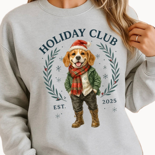 Person wearing a gray sweatshirt with a holiday-themed design featuring a dog and 'Holiday Club' text, standing in front of a decorated Christmas tree.