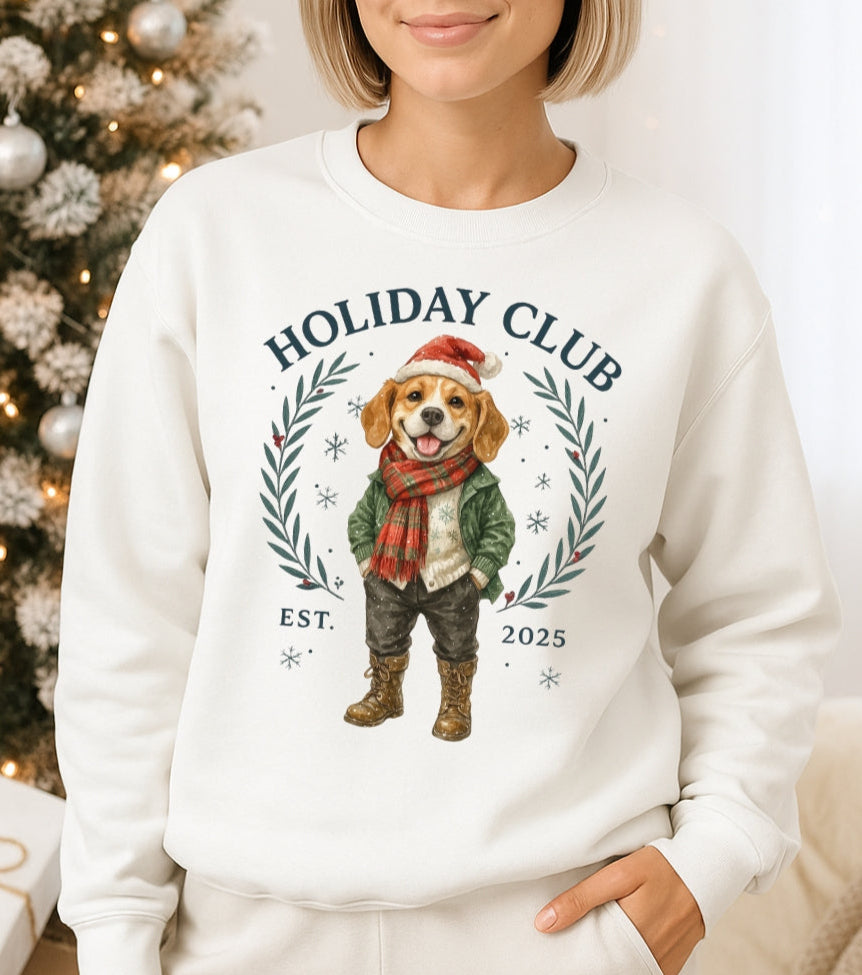 Person wearing a white sweatshirt with a dog graphic and 'Holiday Club' text, standing in front of a decorated Christmas tree.
