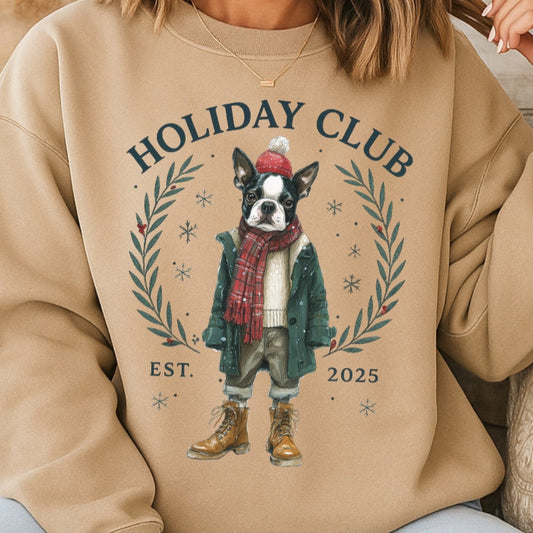 Person wearing a beige sweatshirt with 'Holiday Club' design featuring a dog, sitting on a wooden floor.