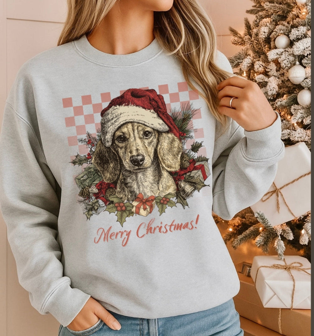 Person wearing a Christmas-themed sweatshirt with a dog design and 'Merry Christmas!' text, standing in front of a decorated Christmas tree.