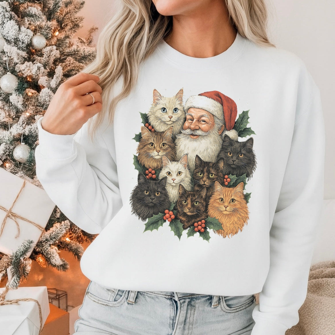 Person wearing a white sweatshirt with a Christmas-themed design of Santa Claus and cats, standing in front of a decorated Christmas tree.