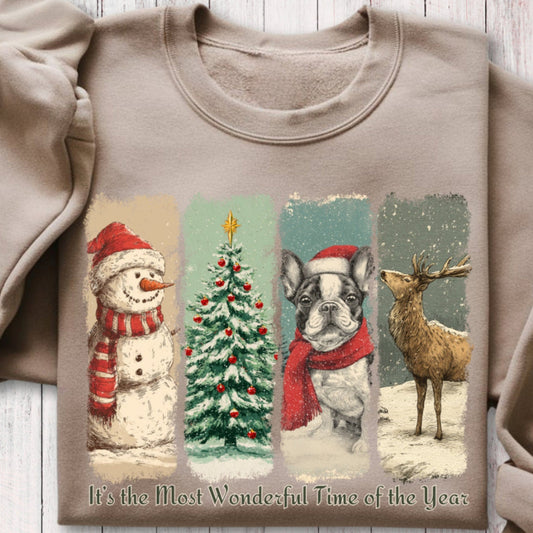 Sand color sweatshirt with Christmas-themed design featuring snowman, tree, frenchie dog, and deer on a wooden surface.