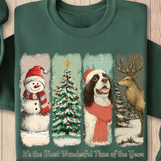 Green sweatshirt with Christmas-themed design featuring a vintage snowman, tree, springer spaniel dog, and deer on a wooden surface.