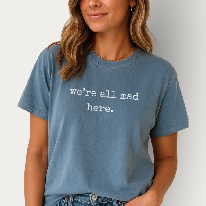 Person wearing a blue t-shirt with 'we're all mad here.' text on a plain background