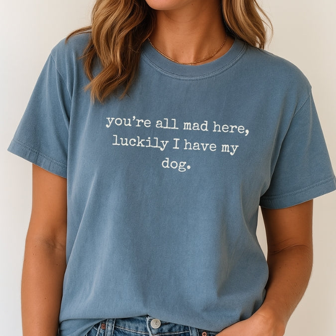Person wearing a blue t-shirt with text 'you're all mad here, luckily I have my dog.'