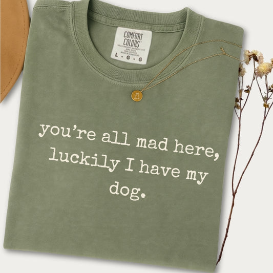 Sage Comfort Colors t-shirt with text 'you're all mad here, luckily I have my dog.' on a white background